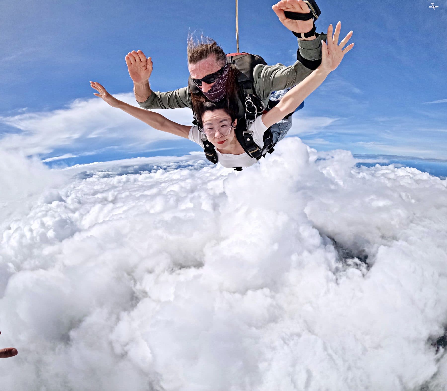 Tandem pair with arms spread, falling toward a bank of white clouds